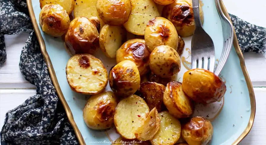 Patate novelle al forno dorate e croccanti, servite su un piatto azzurro con forchetta.