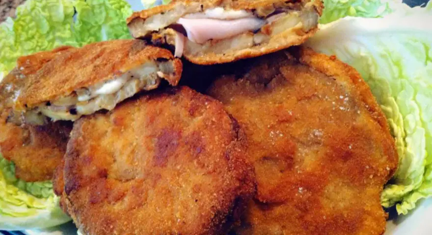 Cordon bleu di melanzane impanati e fritti, ripieni di prosciutto e formaggio filante, serviti su un letto di lattuga croccante.