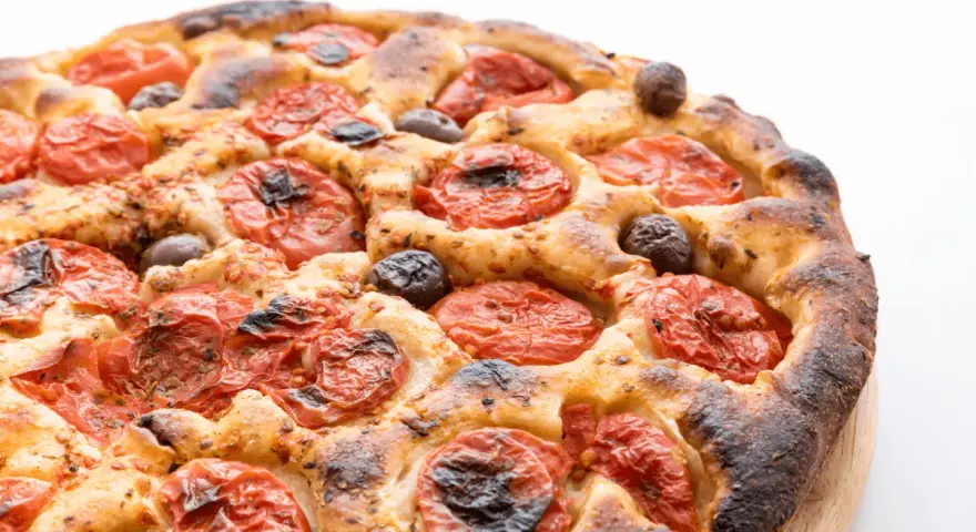Focaccia barese dorata e fragrante, con pomodorini succosi e olive nere, pronta per essere gustata.