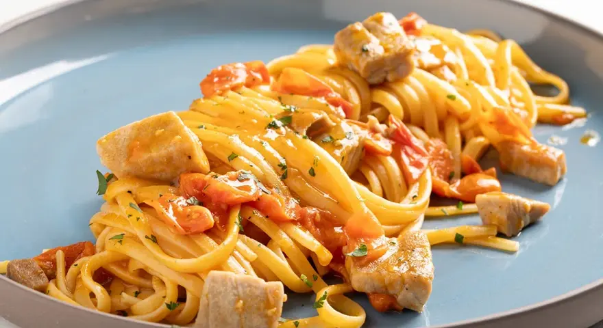 Un piatto invitante di pasta con tonno fresco, pomodorini e prezzemolo, condito con una salsa dorata.
