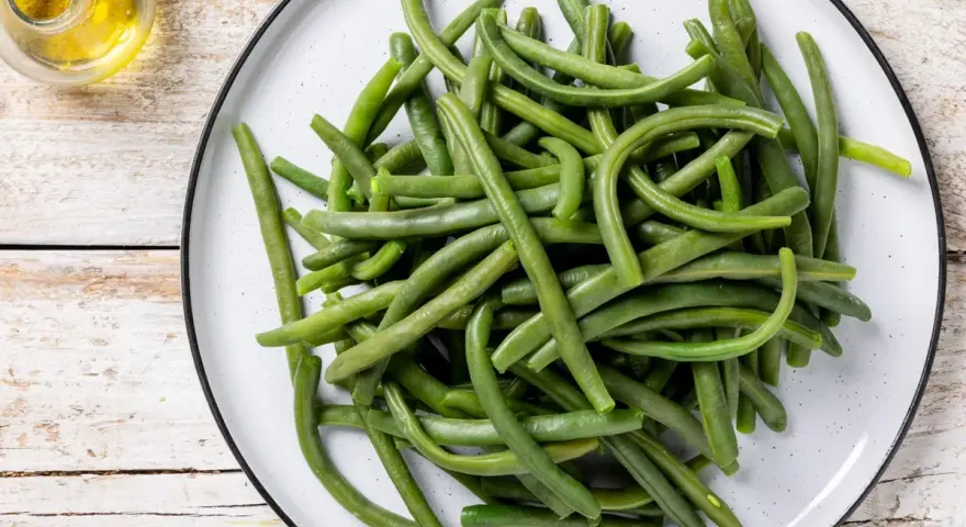 Un piatto di fagiolini lessi, freschi e verdi, pronti per essere gustati. Accanto, un piccolo recipiente con olio d'oliva.