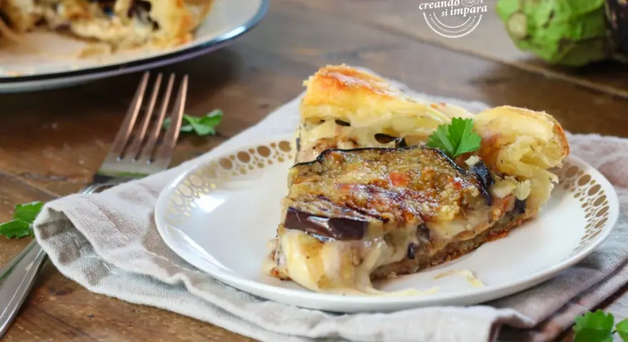 Una fetta di torta salata con melanzane, formaggio filante e pasta sfoglia dorata, guarnita con prezzemolo fresco.