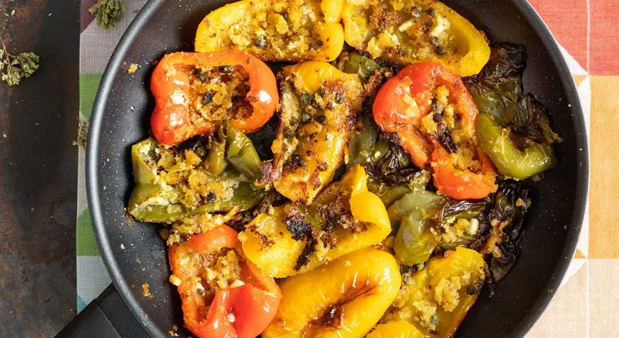Peperoni ammollicati cotti in padella, ripieni di pangrattato e erbe aromatiche, con colori vivaci.