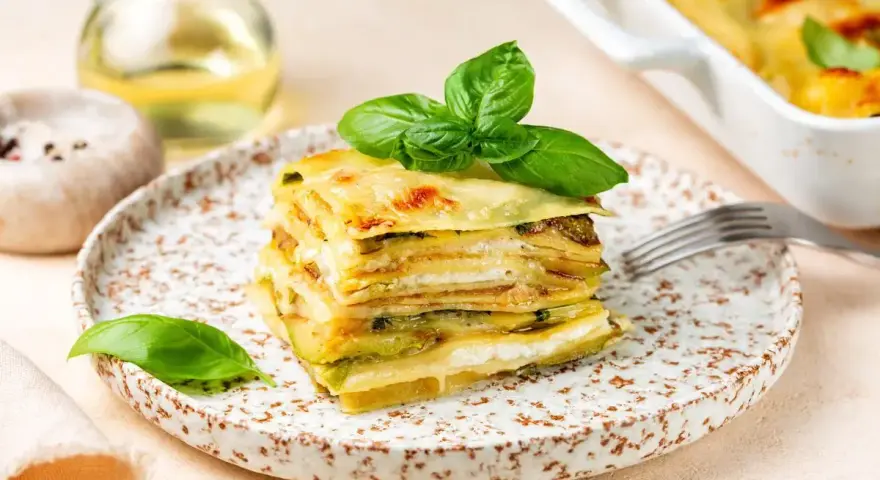 Una fetta di parmigiana di zucchine, stratificata e dorata, guarnita con basilico fresco.