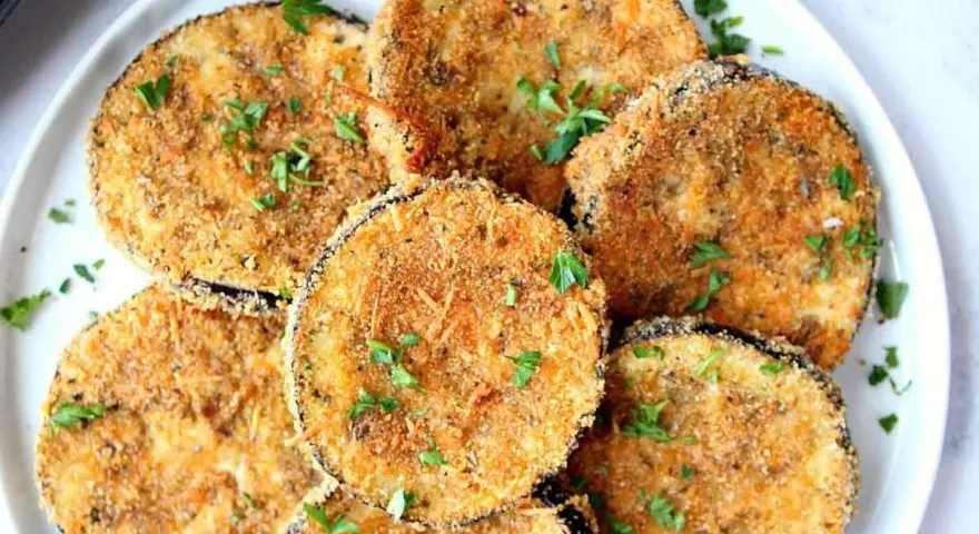 Fette dorate di melanzane impanate al forno, guarnite con prezzemolo fresco. Un antipasto croccante e saporito.