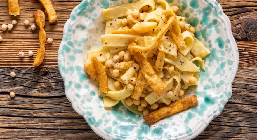 Piatto di ciceri e tria, pasta fresca con ceci e croccanti sfoglie fritte, servito in un piatto decorato.