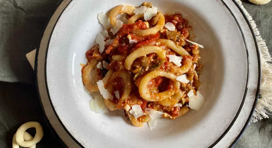 Un piatto di anellini alla pecorara, pasta a forma di anello condita con sugo di pomodoro, verdure e scaglie di formaggio.
