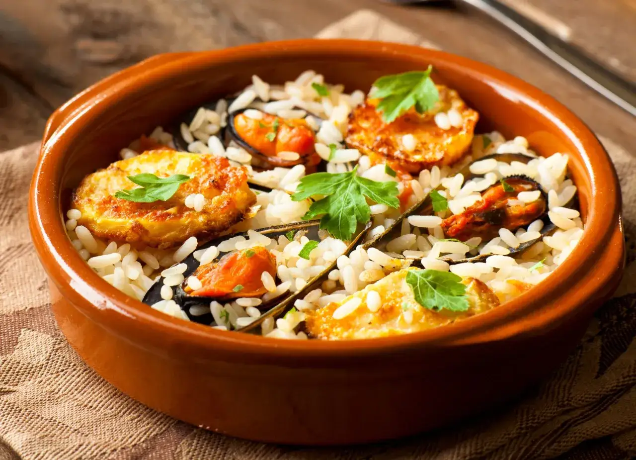Piatto di riso patate e cozze, guarnito con prezzemolo fresco, servito in una ciotola di terracotta.