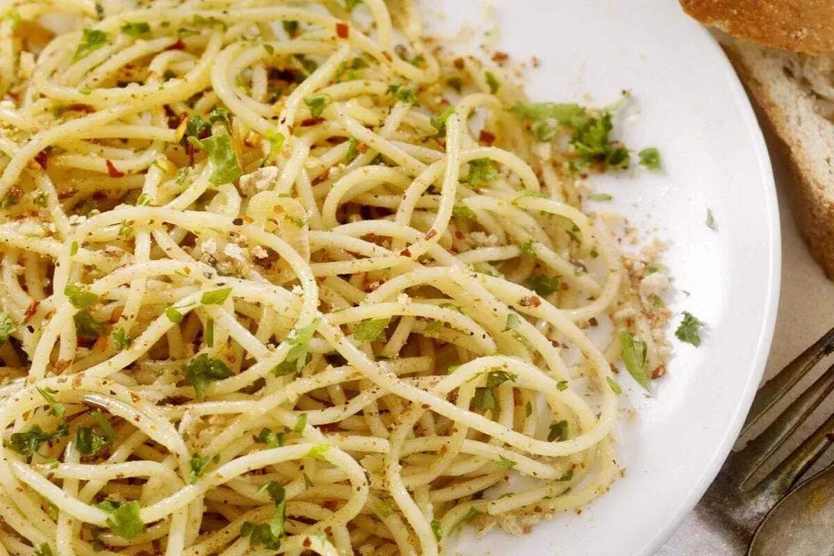 Un piatto di spaghetti alla carrettiera, conditi con aglio, olio, peperoncino e prezzemolo fresco, accompagnati da pane rustico.