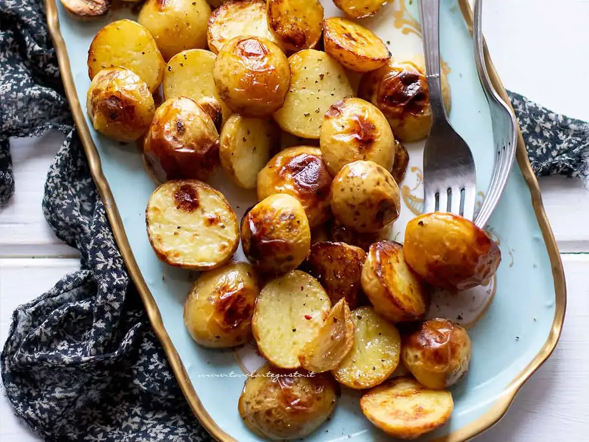 Patate novelle al forno dorate e croccanti, servite su un piatto decorato con un tovagliolo scuro.