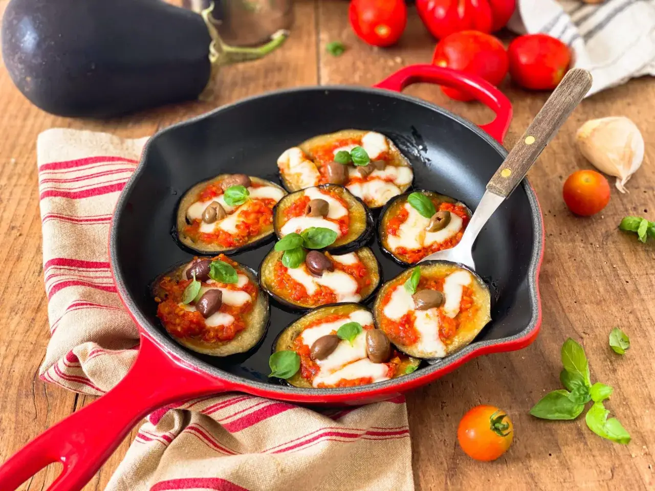 Melanzane in padella con pomodoro e mozzarella, guarnite con olive e basilico. Un antipasto invitante e saporito.