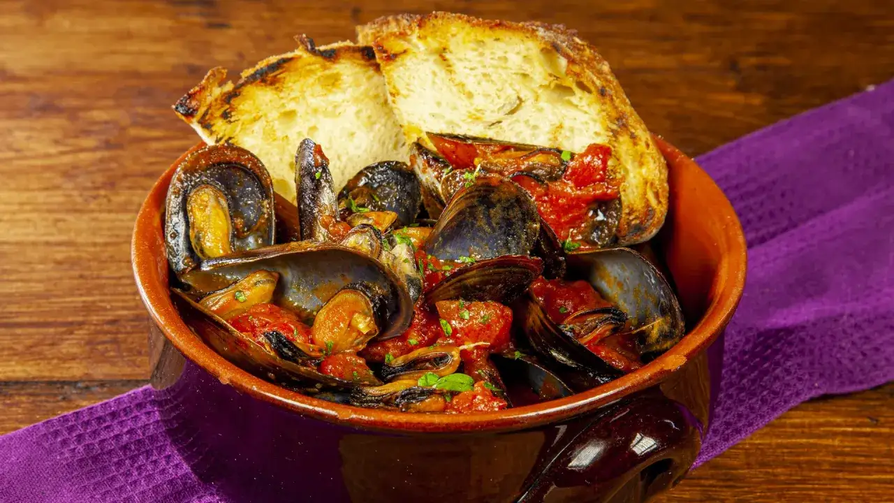 Cozze alla tarantina ricetta: un piatto fumante di cozze in salsa di pomodoro, servito con pane tostato.