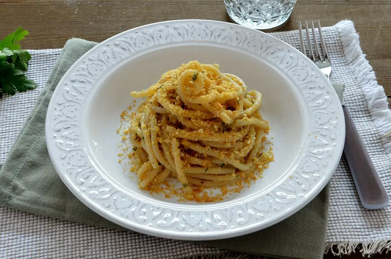 Spaghetti con acciughe e pangrattato, un piatto semplice ma gustoso, servito in un piatto bianco decorato.