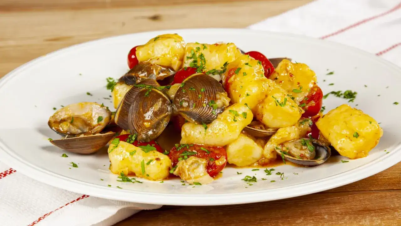 Gnocchi di patate con vongole e pomodorini, un piatto saporito e colorato, guarnito con prezzemolo fresco.