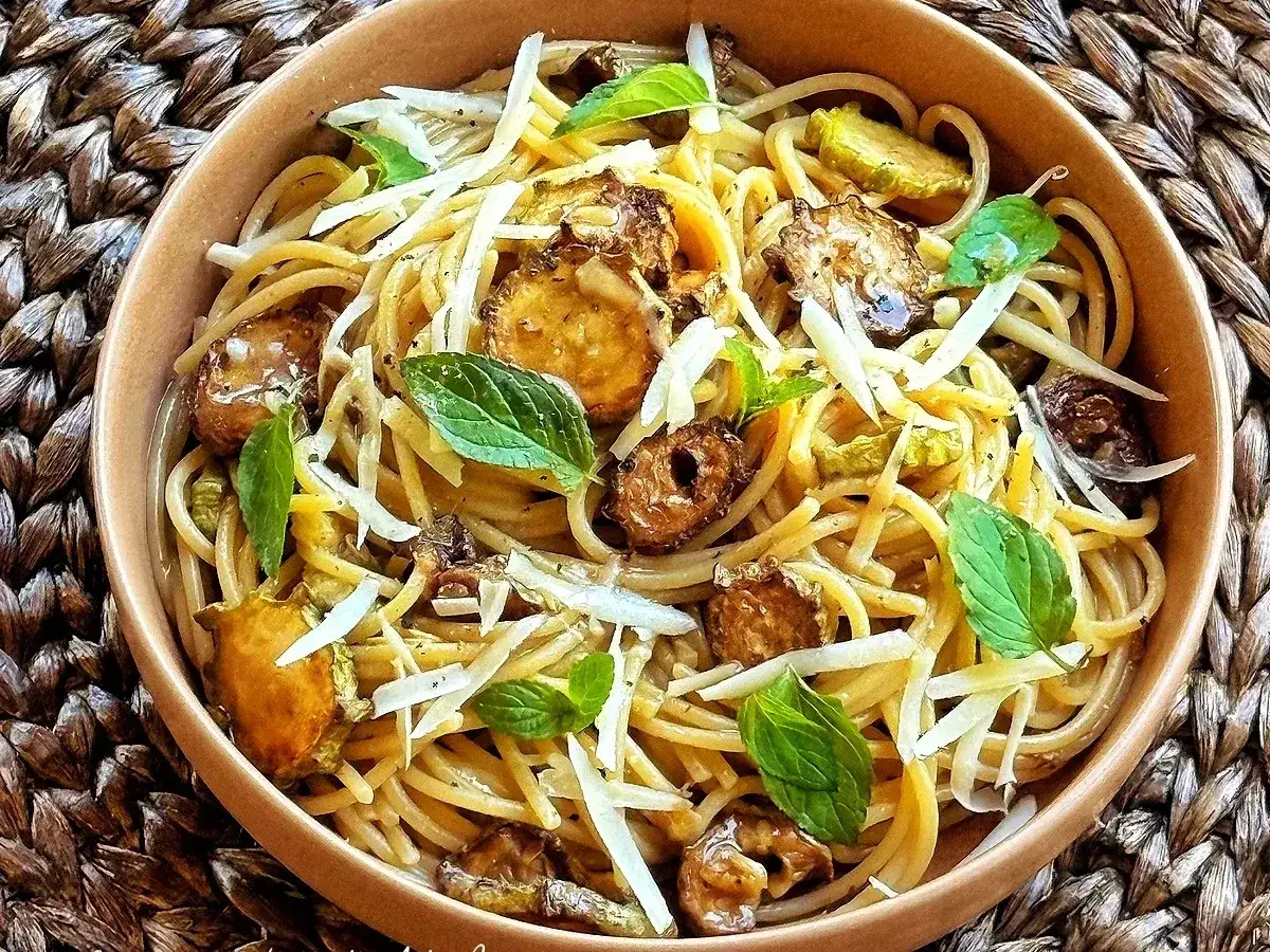 Spaghetti di zucchine fritte croccanti, guarniti con scaglie di parmigiano e foglie di menta fresca. Un piatto leggero e saporito.