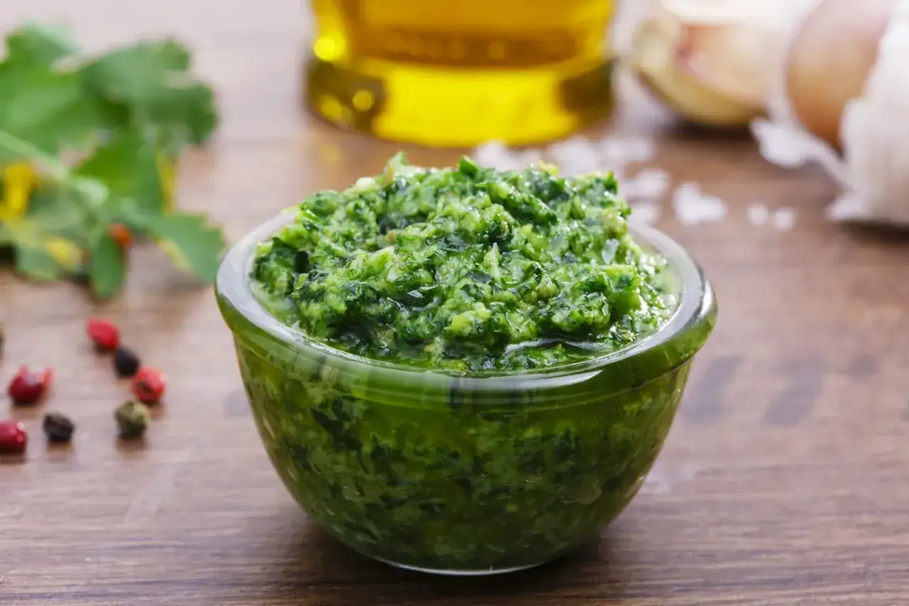 Salsa verde ricetta della nonna in una ciotola di vetro, con ingredienti freschi come aglio, olio e erbe aromatiche sullo sfondo.