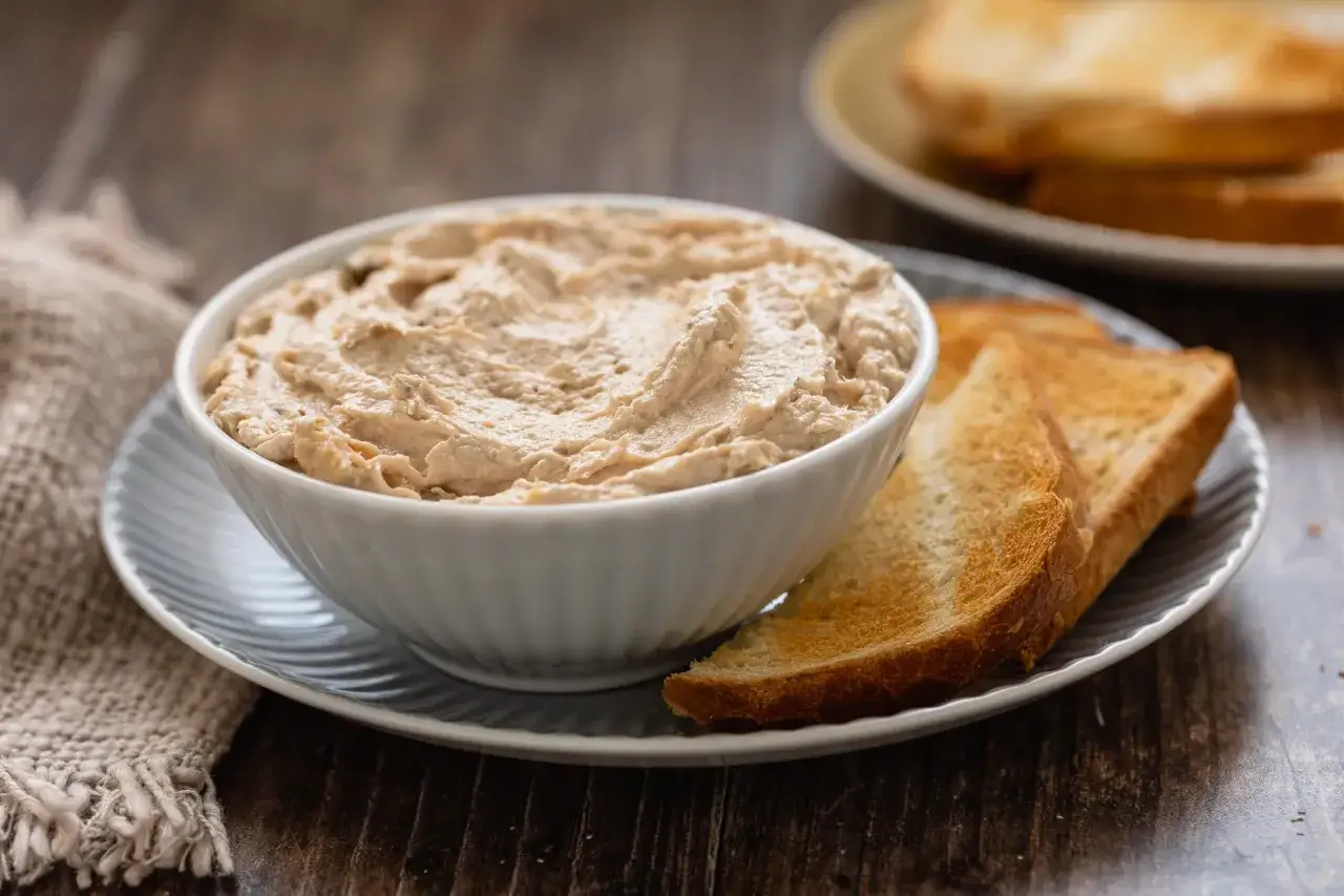 Una ciotola di cremosa mousse di tonno, servita con fette di pane tostato dorato, pronta per essere gustata.