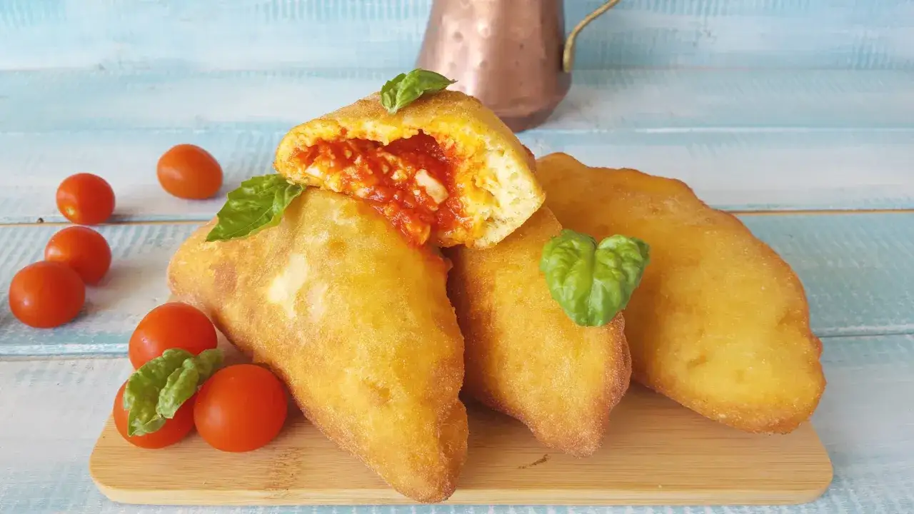 Panzerotti pugliesi dorati e ripieni di pomodoro e mozzarella, guarniti con basilico fresco e pomodorini.