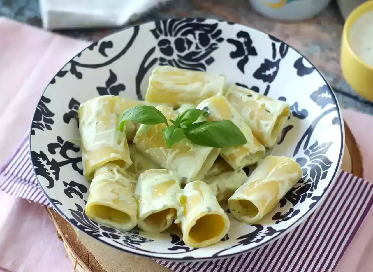 Piatto di paccheri conditi con una cremosa salsa alla ricotta, guarnito con basilico fresco. La pasta con ricotta ricetta della nonna, un classico intramontabile.