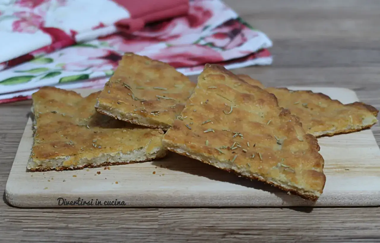 Fette di focaccia senza lievito, dorate e profumate al rosmarino, servite su un tagliere di legno.