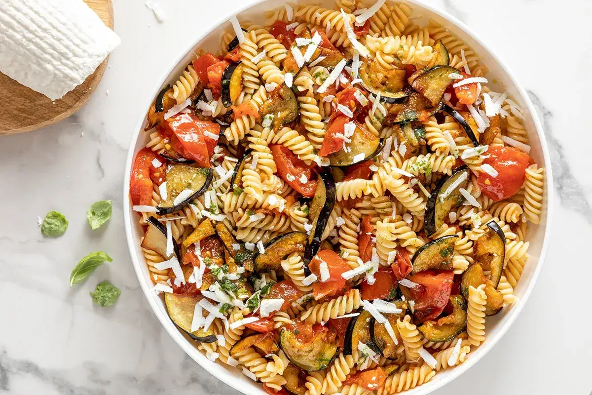 Un piatto invitante di pasta fredda alla norma, con melanzane, pomodori e ricotta salata grattugiata.