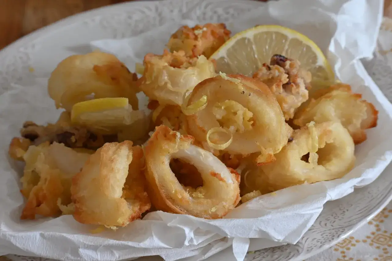 Un piatto di calamari fritti dorati, croccanti e invitanti, guarniti con spicchi di limone fresco e scorzette.