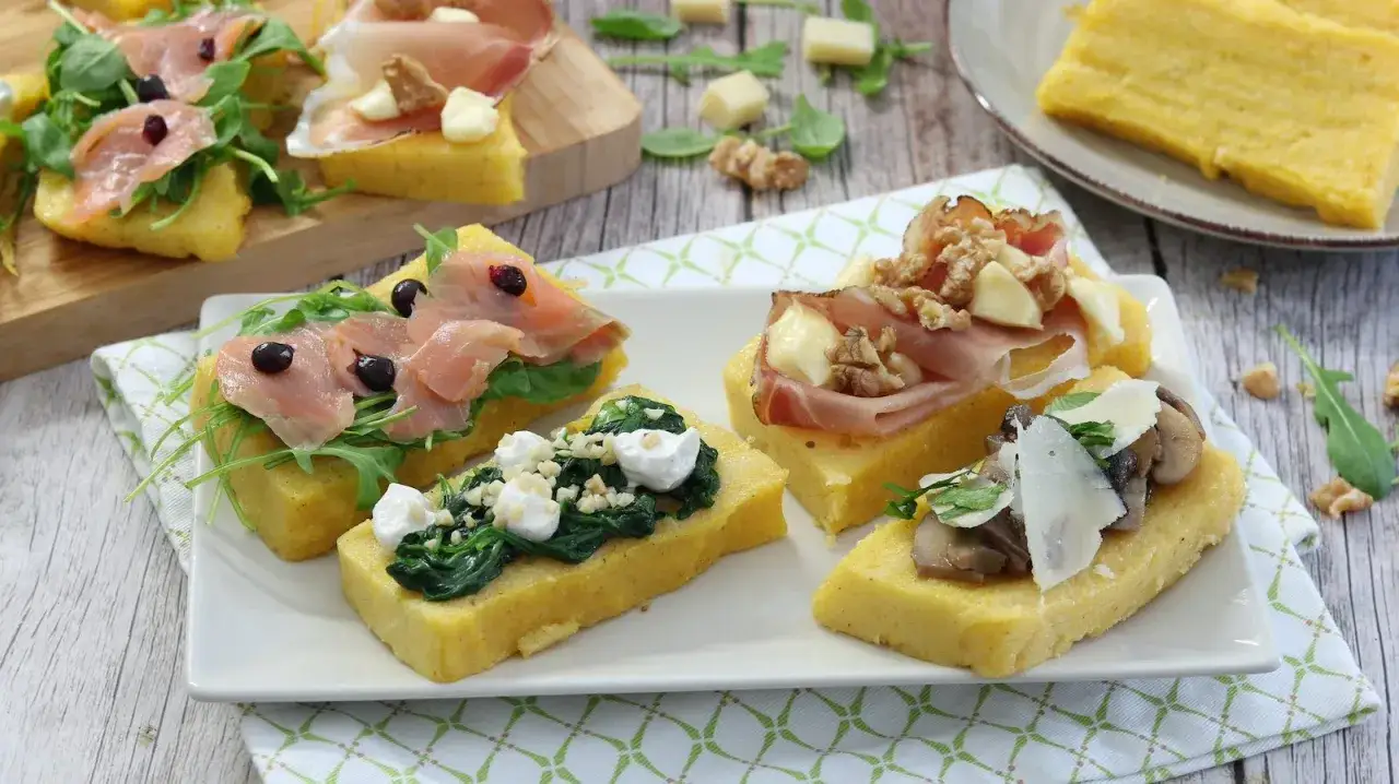 Deliziosi crostini di polenta misti con salmone, spinaci, prosciutto e funghi. Un antipasto colorato e gustoso.