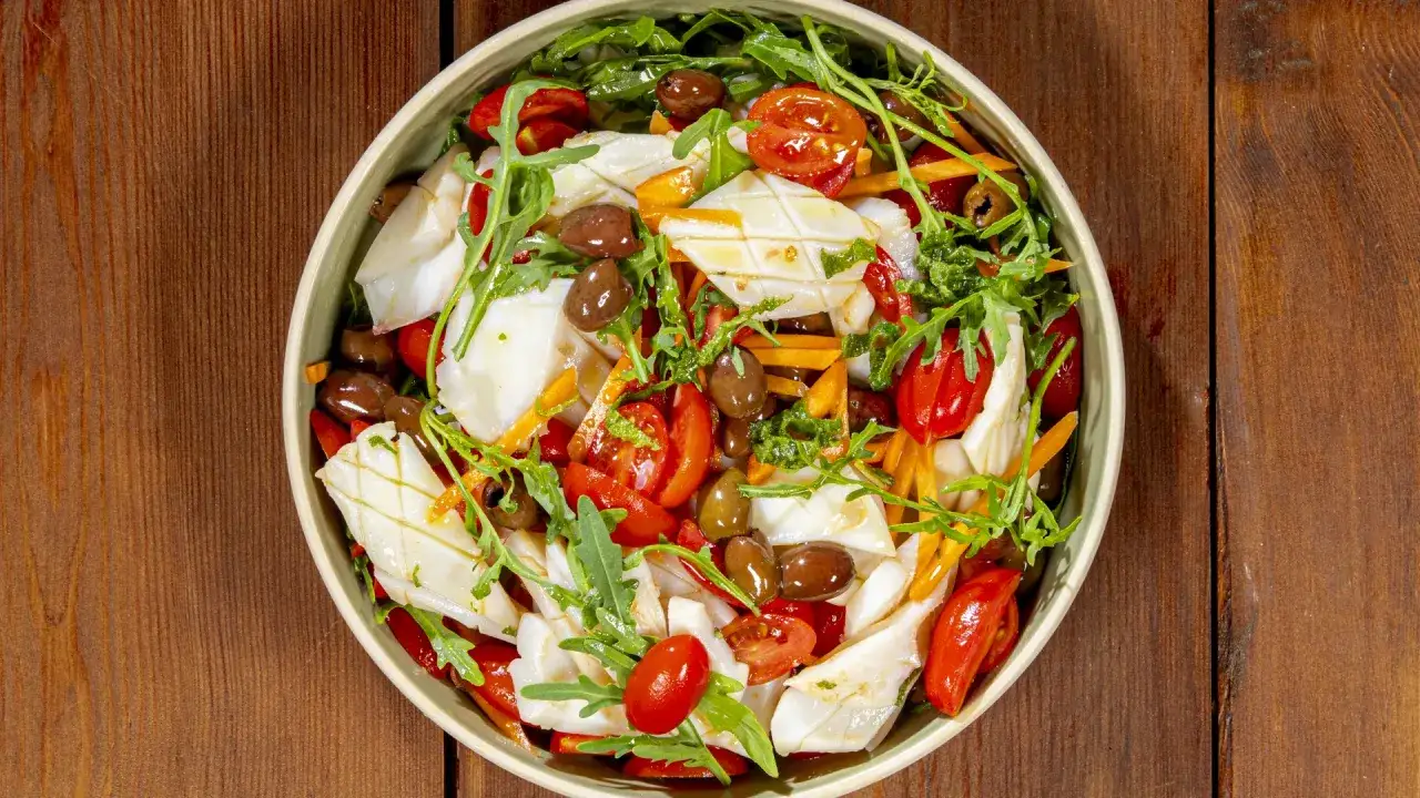 Insalata di calamari fresca con pomodorini, olive, rucola e carote julienne, un piatto leggero e gustoso.