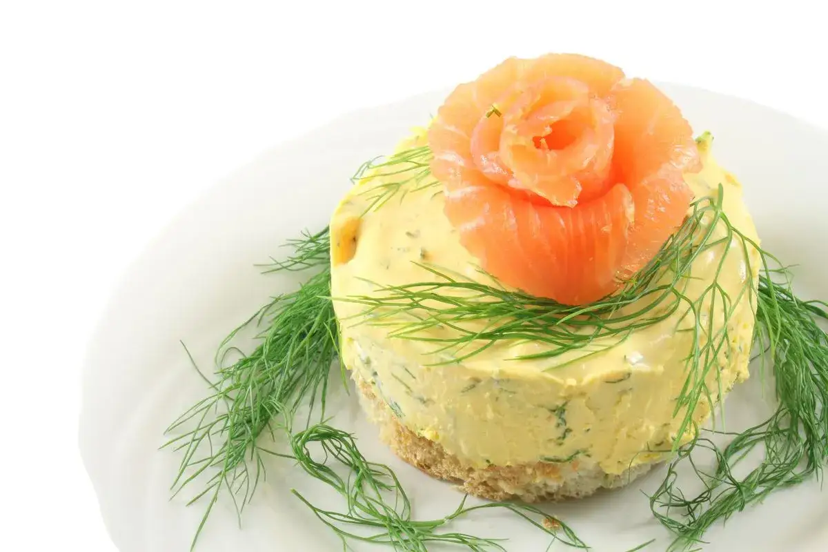Cheesecake salata al salmone, decorata con un fiore di salmone affumicato e aneto fresco, su una base croccante.
