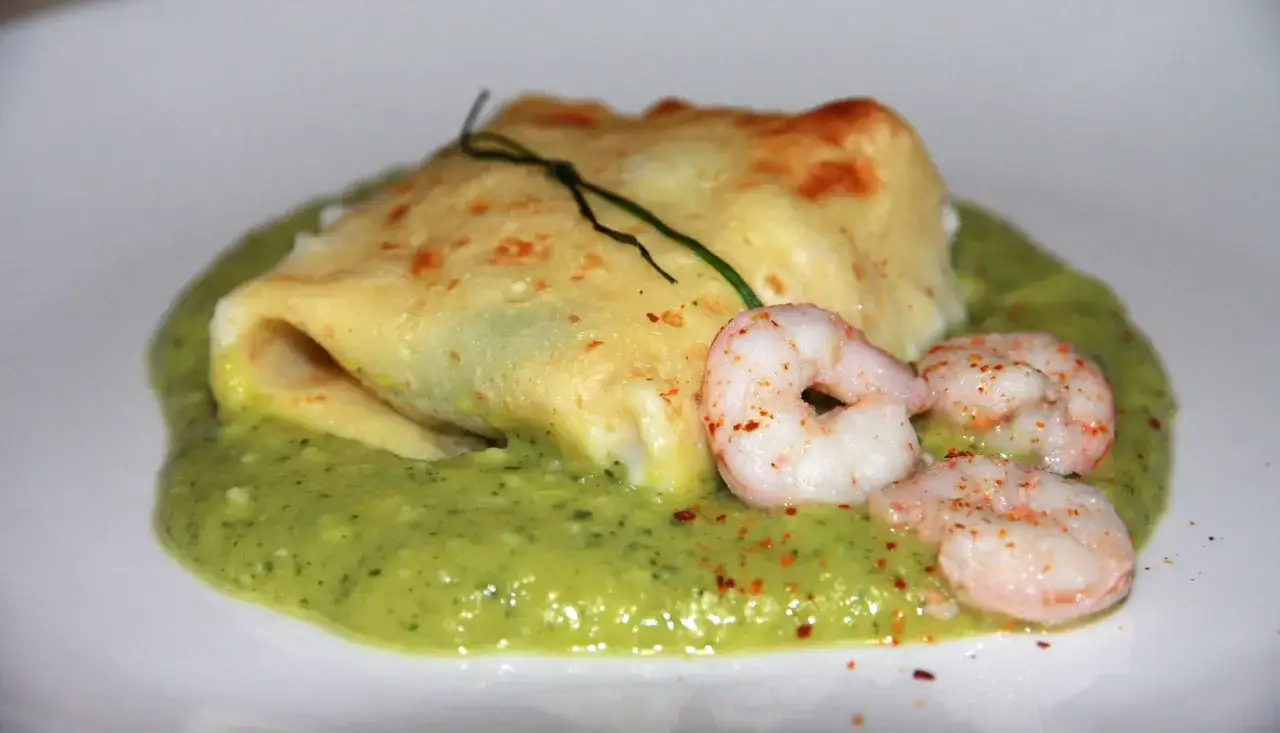 Crepes di zucchine ripiene, servite su una crema verde e guarnite con gamberi e peperoncino.