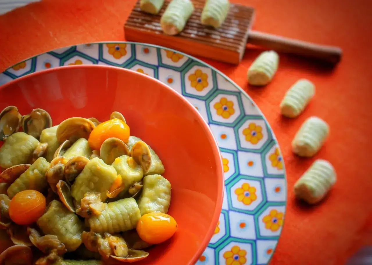 Gnocchi al pesto e vongole, un piatto colorato e gustoso, con pomodorini e cozze fresche.