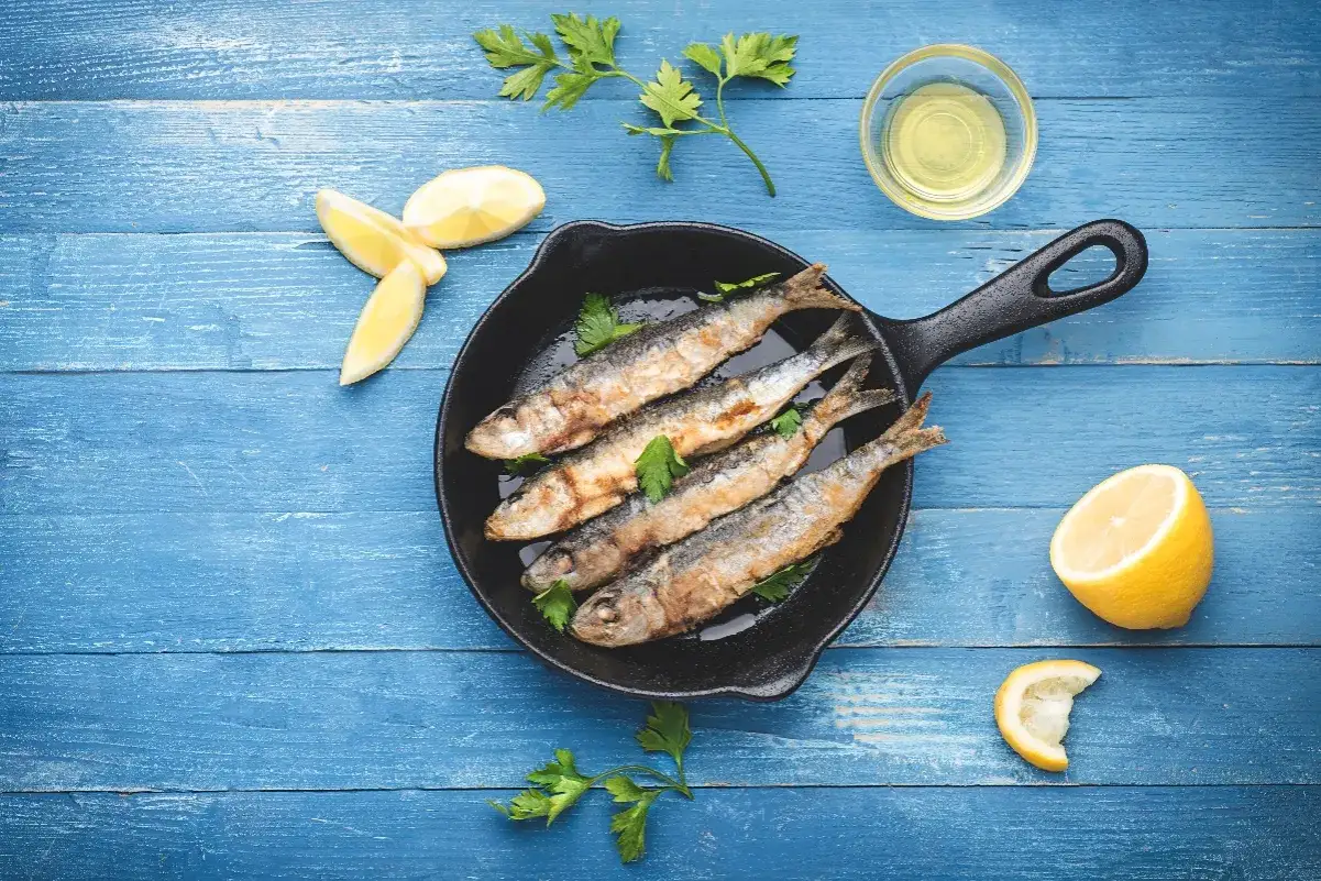 Alici in padella dorate e croccanti, guarnite con prezzemolo fresco, pronte per essere gustate con spicchi di limone.