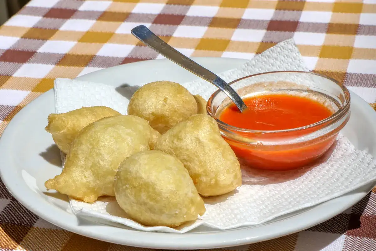 Pittule salentine dorate e croccanti, servite con una ciotolina di salsa rossa.