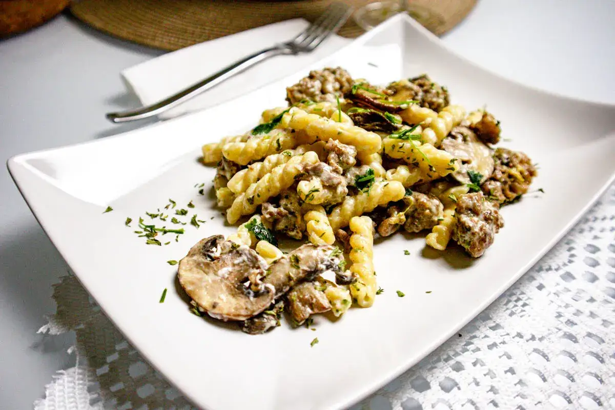 Un piatto di pasta salsiccia e funghi, condito con prezzemolo fresco, servito su un piatto bianco.