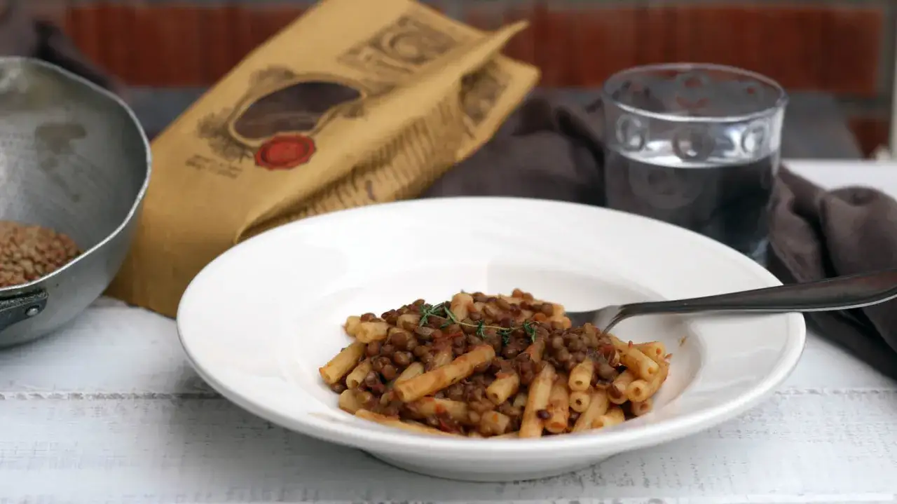 Piatto di pasta con rag&ugrave; di lenticchie, un classico confortante. Accanto, un bicchiere d'acqua e una confezione di lenticchie.
