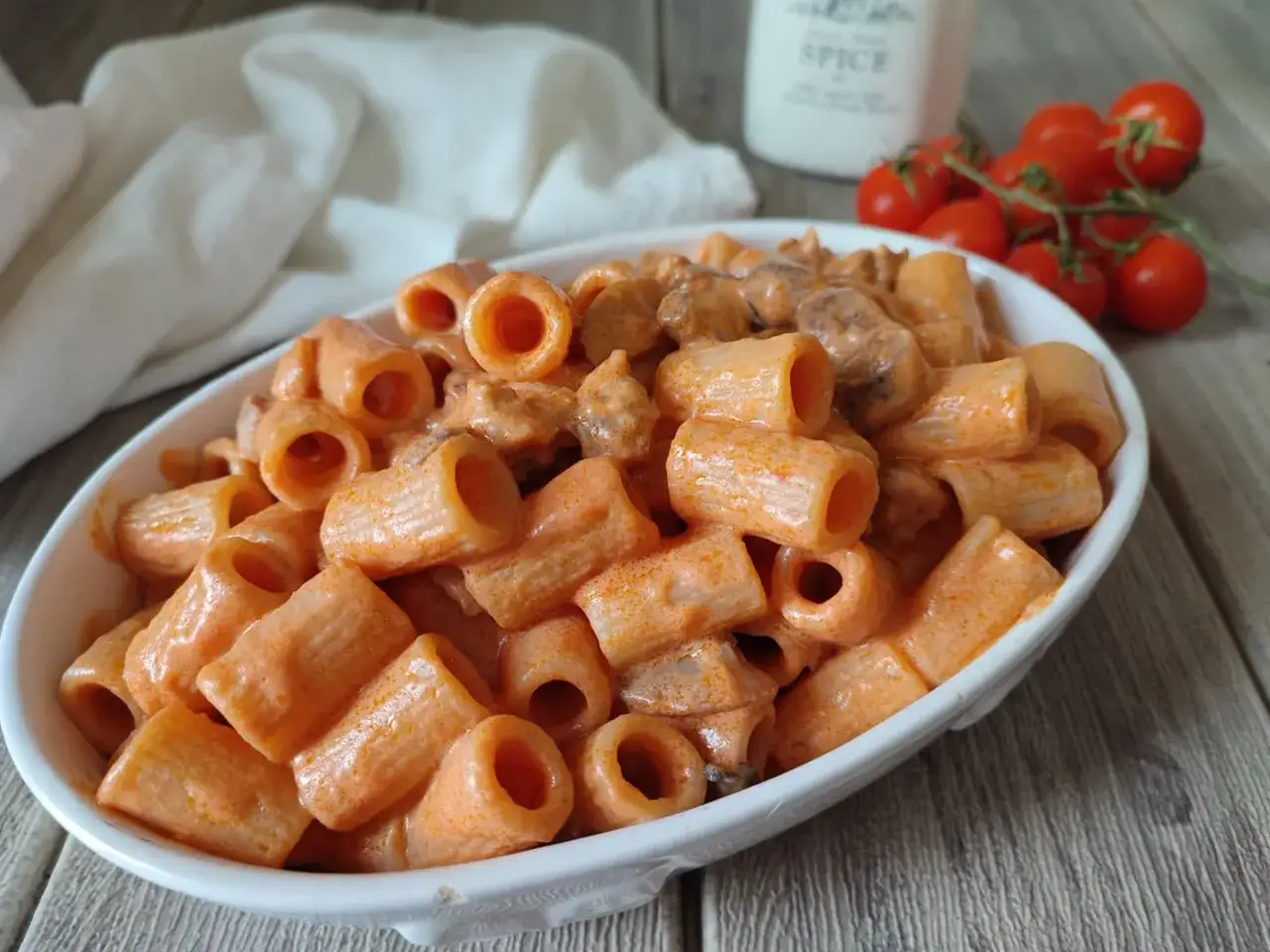 Un piatto invitante di pasta alla carcerata, con rigatoni conditi in una cremosa salsa rossa, accompagnato da pomodorini freschi.