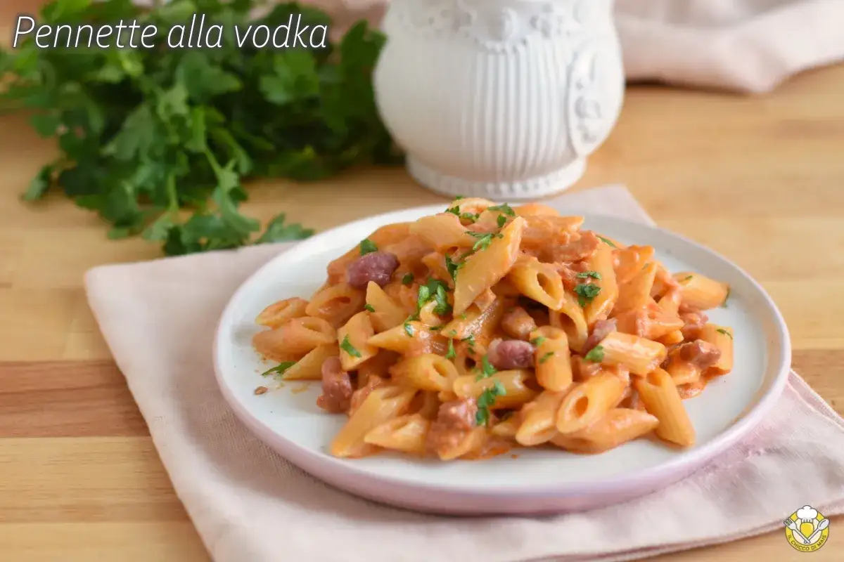 Piatto di penne alla vodka cremose, guarnite con prezzemolo fresco e pezzetti di salame.