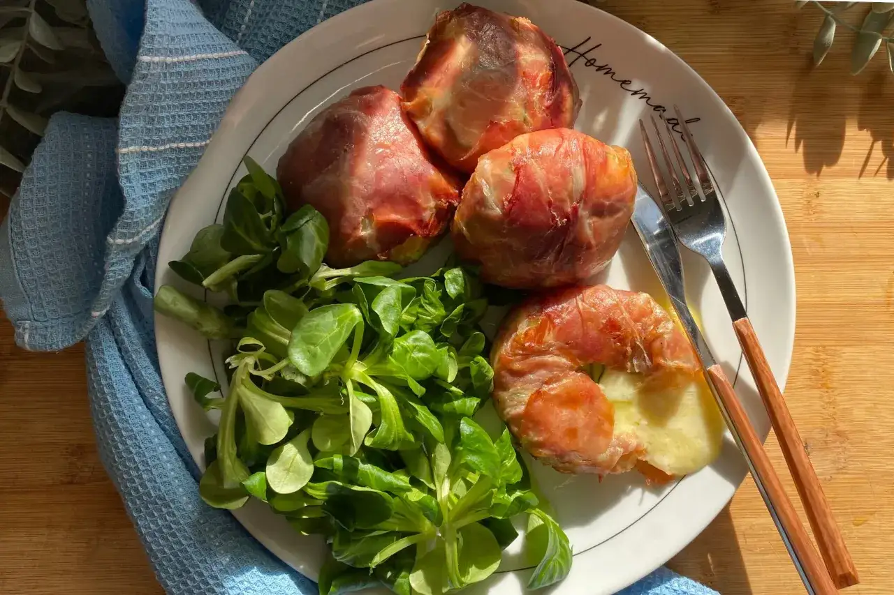 Piatto con involtini di prosciutto e formaggio tomino fuso, accompagnati da insalata fresca.