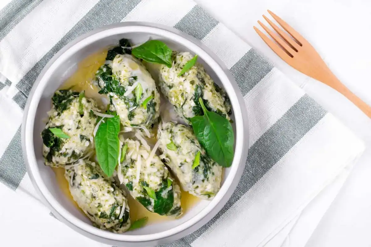 Gnudi ricetta: deliziosi gnocchetti di ricotta e spinaci in un piatto bianco, guarniti con formaggio grattugiato e foglie fresche.