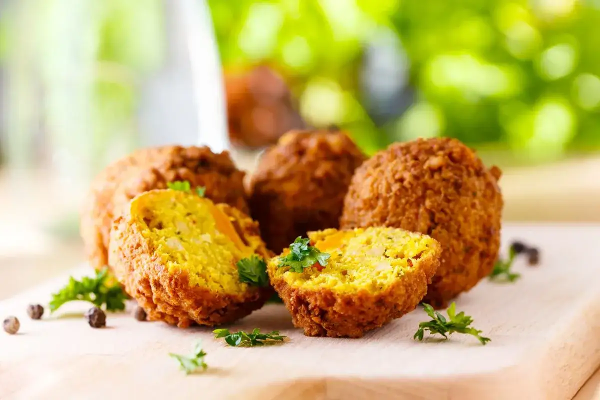 Polpette di ceci dorate e croccanti, cotte in friggitrice ad aria, guarnite con prezzemolo fresco su tagliere di legno.