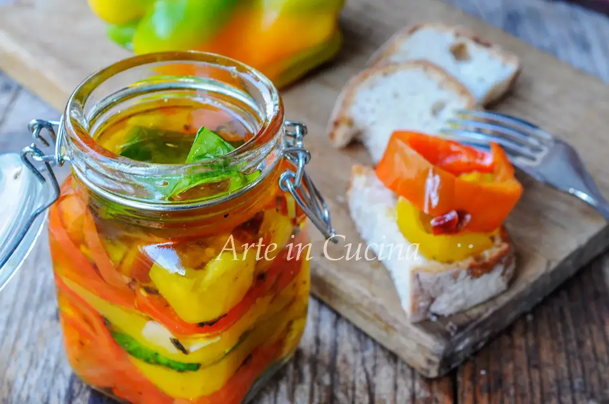 Barattolo di peperoni sott'olio colorati, con basilico fresco. Un crostino con peperoni e pane rustico, pronto per essere gustato.