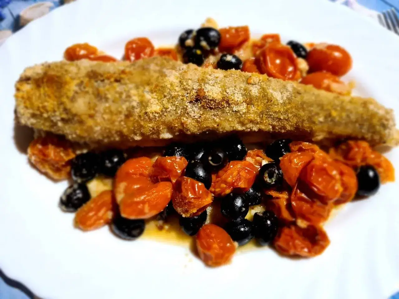 Trancio di palombo impanato su un letto di pomodorini confit e olive nere.