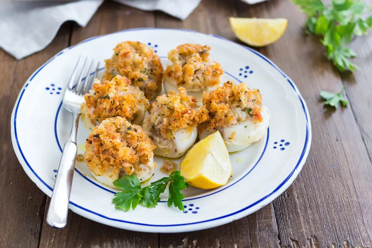 Seppie gratinate al forno, un piatto gustoso con ripieno croccante, servite su un piatto bianco con limone e prezzemolo.