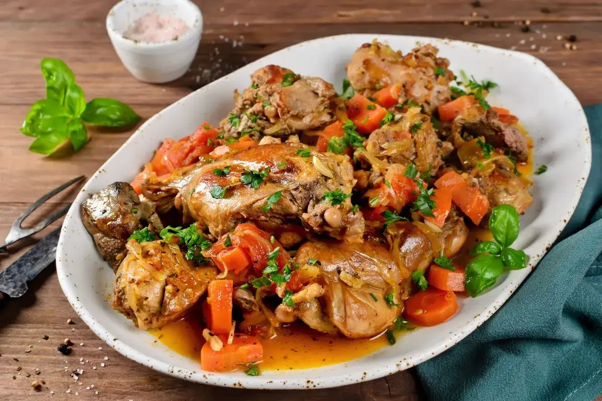 Piatto invitante di coniglio in umido con carote e erbe aromatiche, servito su un vassoio bianco.