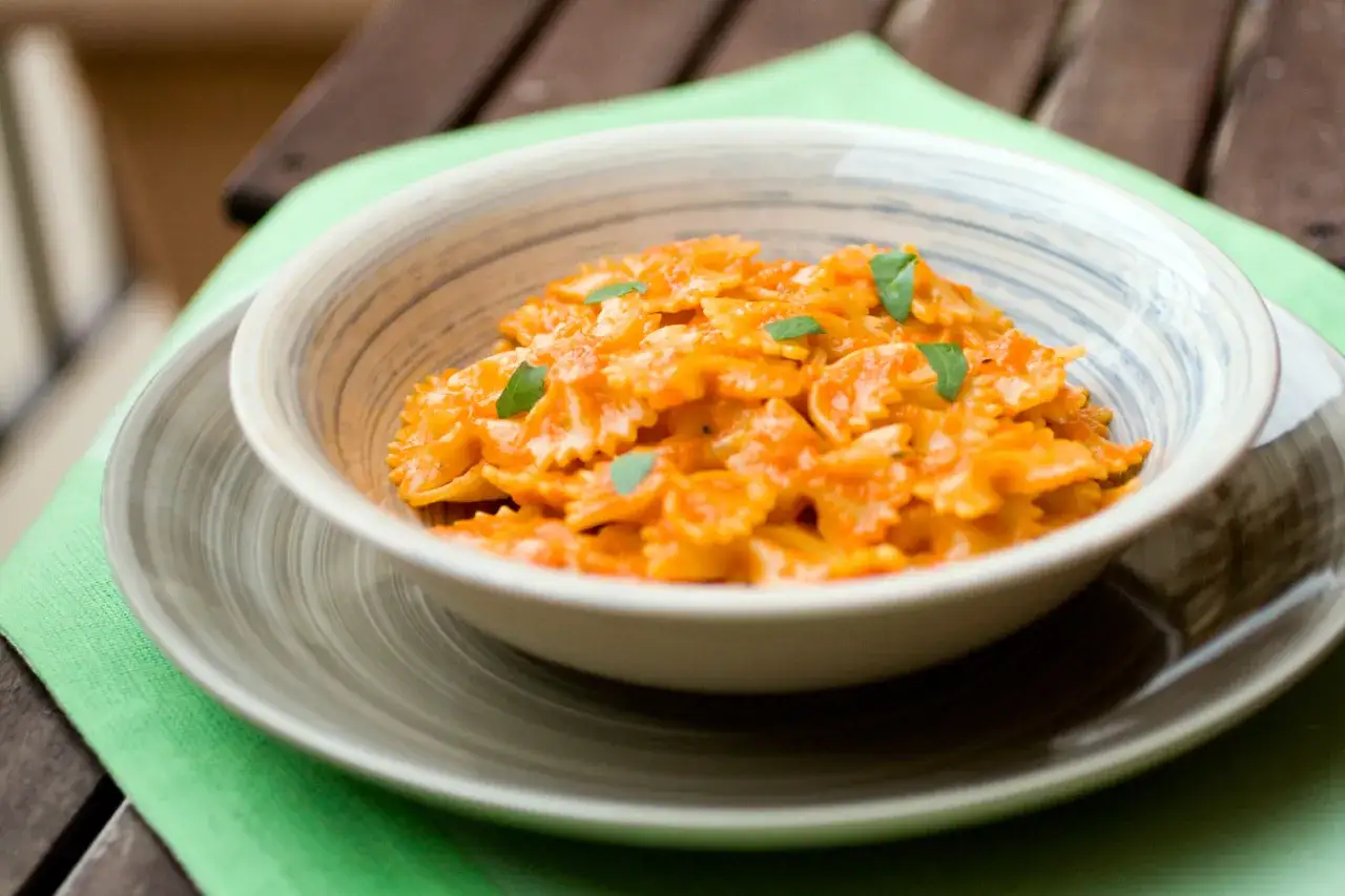 Farfalle condite con una cremosa salsa ai peperoni, guarnite con basilico fresco. Un piatto invitante e saporito.
