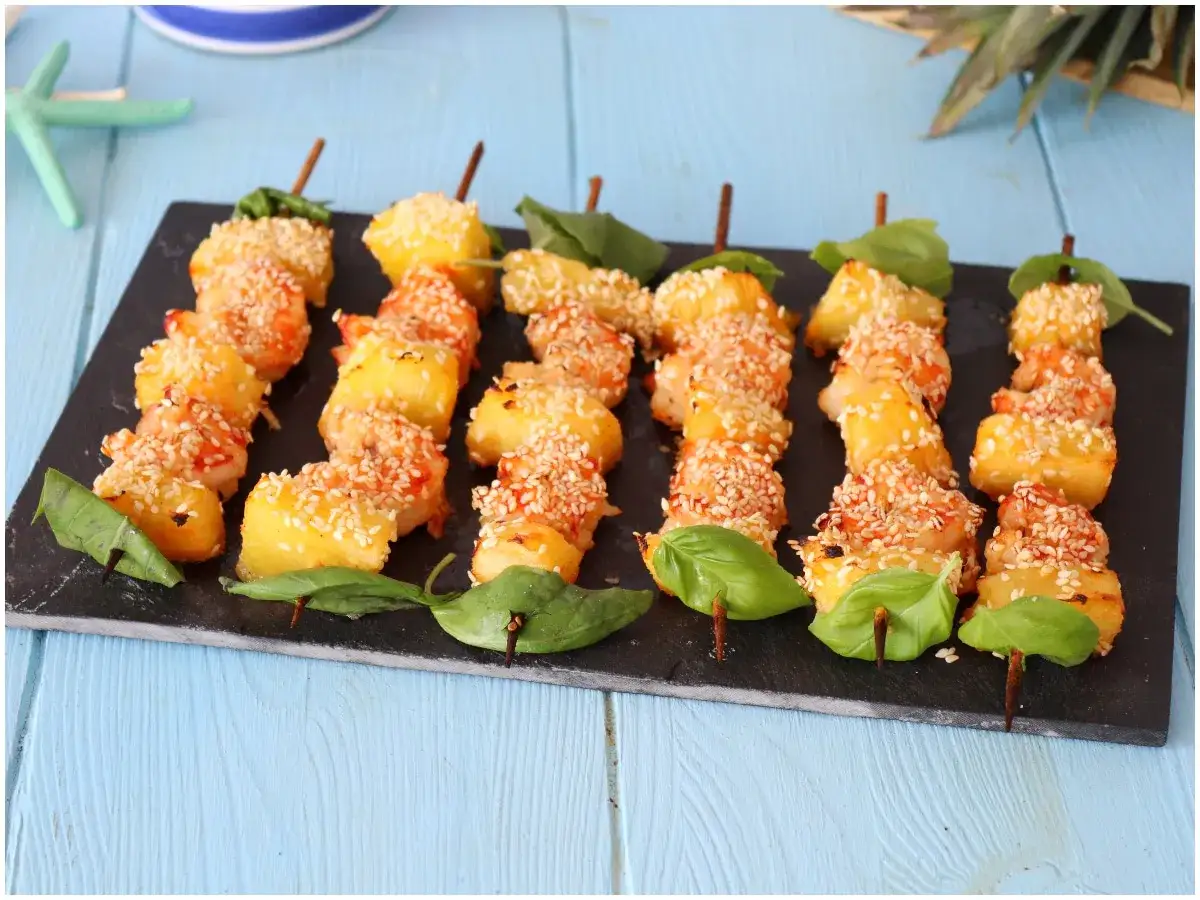 Spiedini per aperitivo veloci con gamberi e ananas, ricoperti di sesamo e guarniti con basilico.