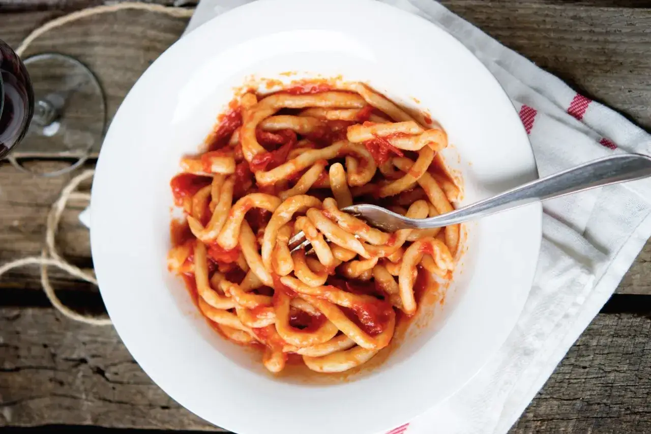 Piatto di pasta fresca condita con un saporito sugo all'aglione, servito su un piatto bianco con una forchetta.