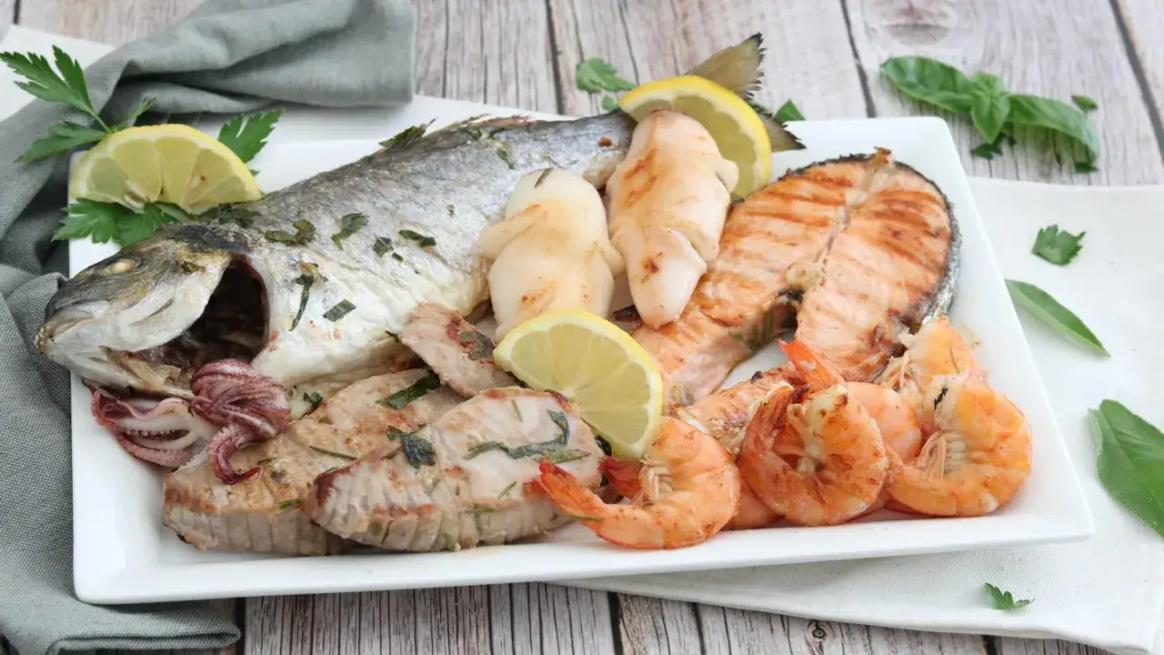 Un piatto invitante di grigliata di pesce: orata intera, tranci di salmone, gamberi, calamari e tonno, guarnito con limone e prezzemolo.