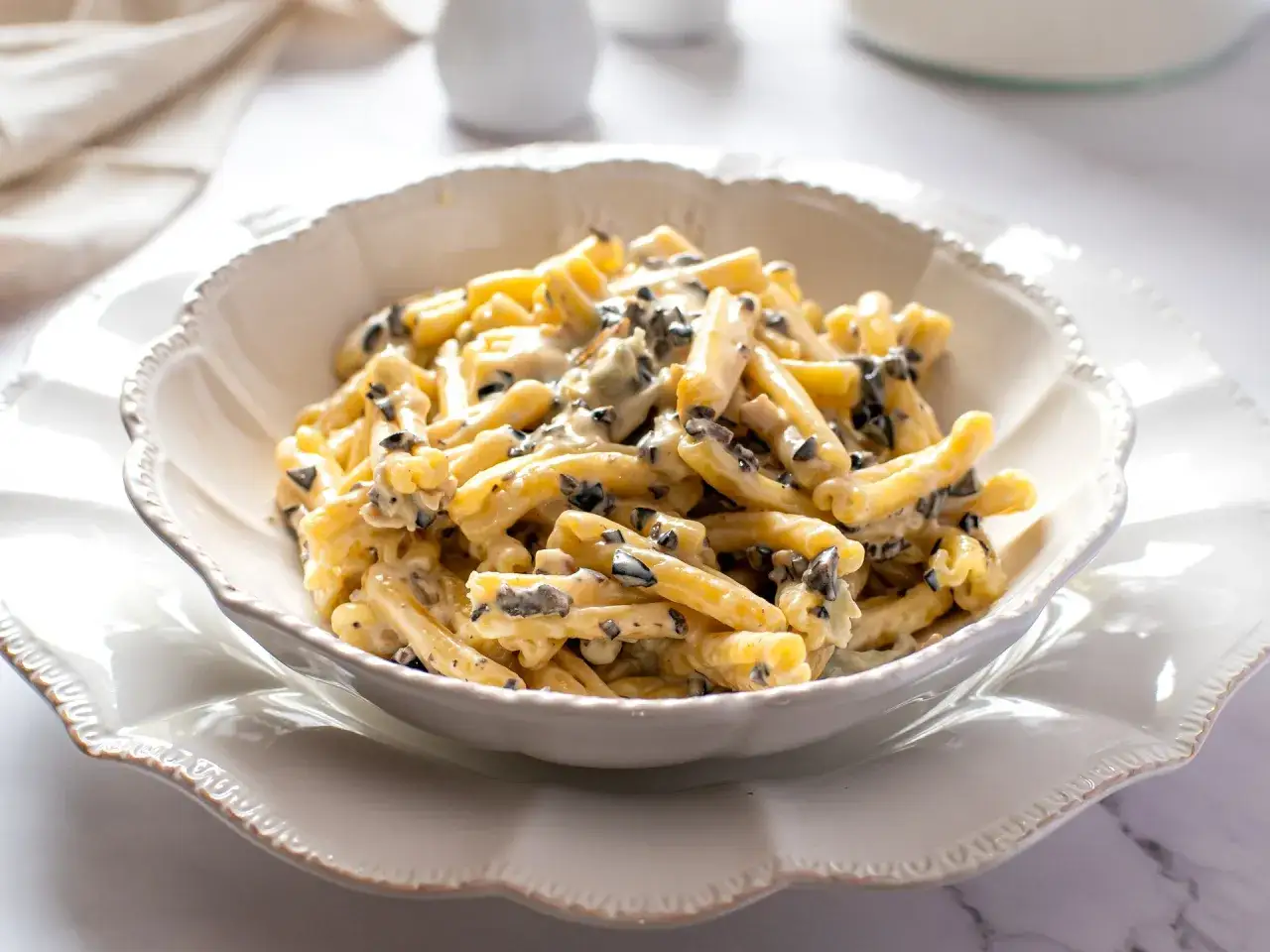Un piatto di pasta alla cenere cremosa, con pezzetti scuri di olive, servita in una ciotola bianca decorata.