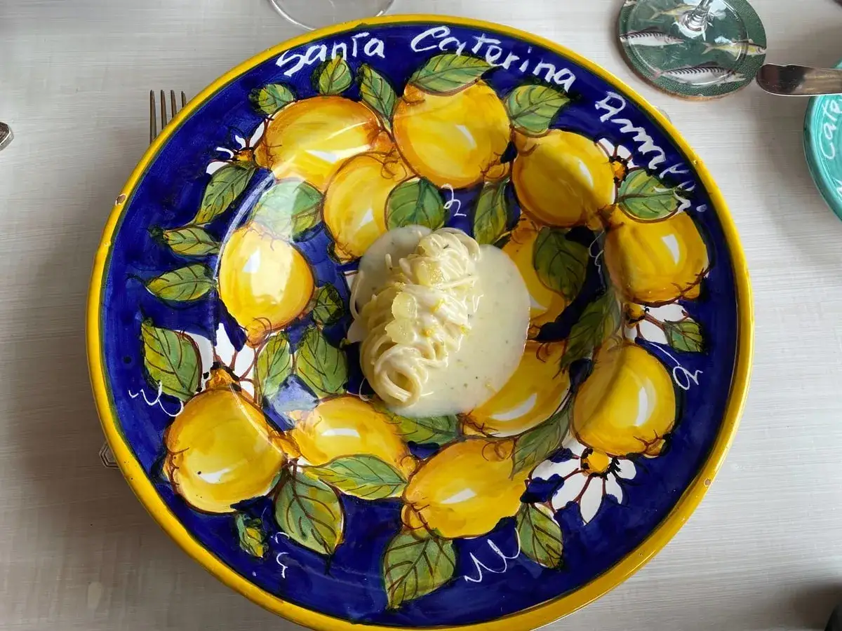 Spaghetti al limone, un piatto profumato che evoca la Costiera Amalfitana, servito su un piatto decorato con limoni e fiori.